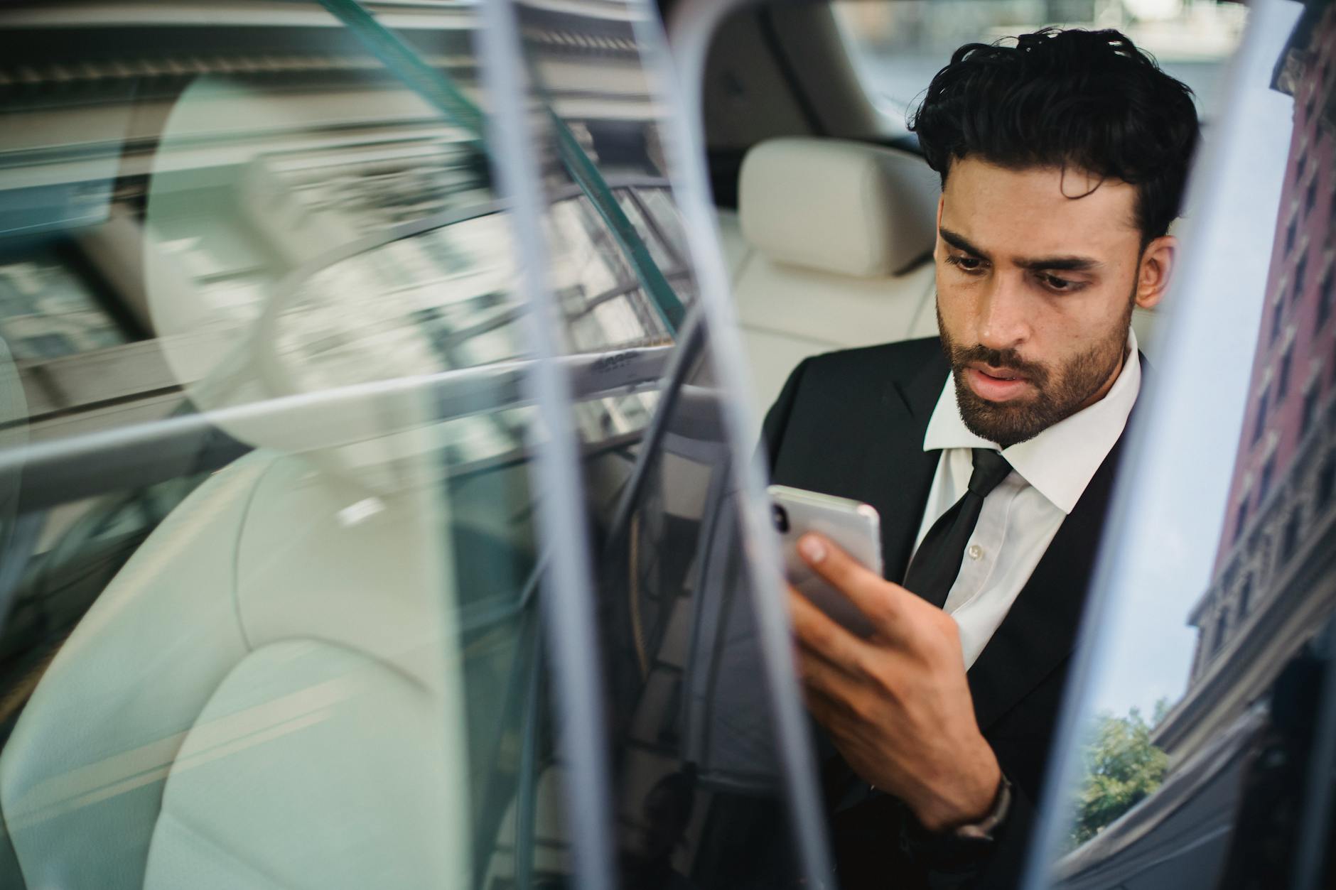 man in black suit holding a smartphone in a car