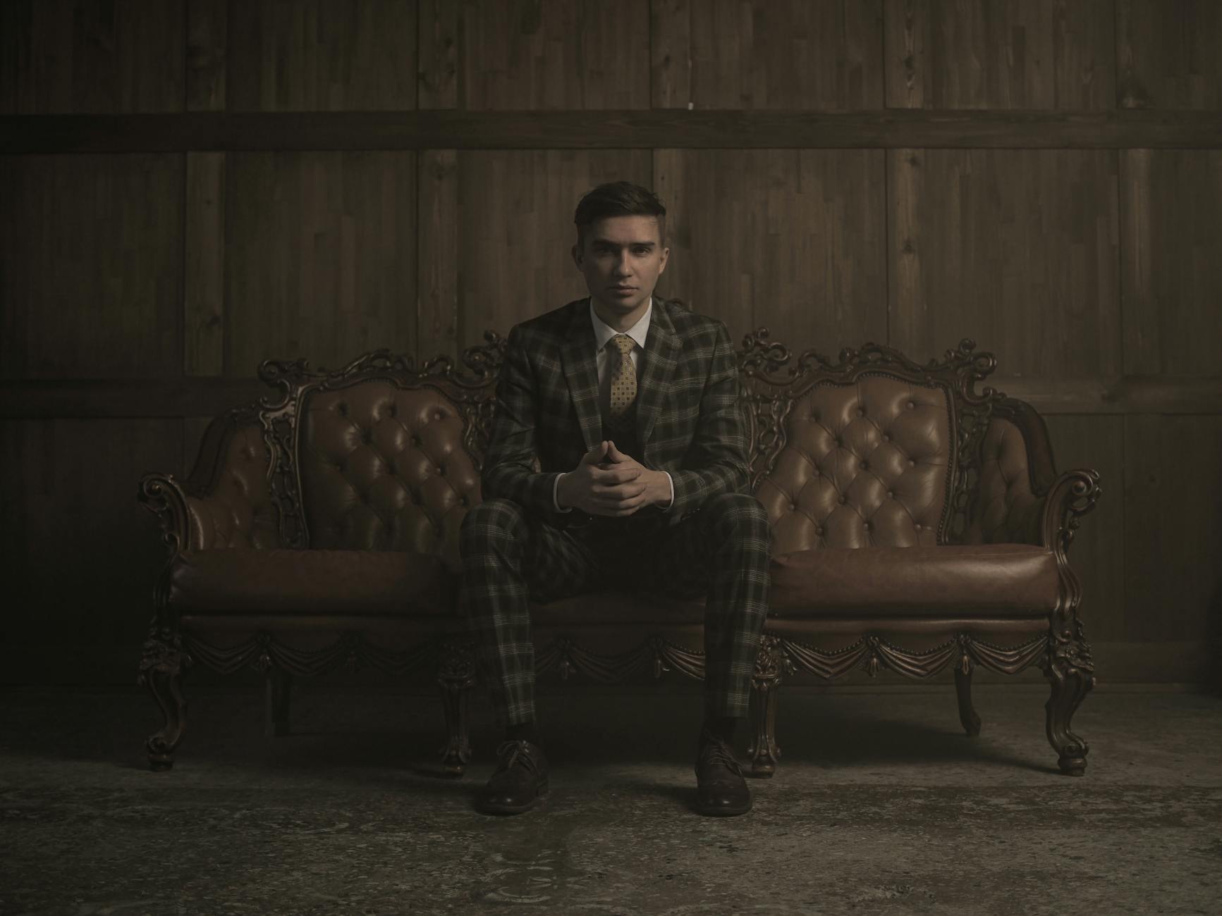 man in suit sitting on sofa dating high-value men, financially struggling man, self-made man vs daddy’s boy, dating advice for women, spotting ambition in men, evaluating character in relationships, high-value provider types, relationship tips for women, navigating dating a provider, dating smart, love over money, choosing the right partner, setting boundaries in relationships, mutual growth in dating, building legacy with partner, high-value relationships guide, dating men with potential, understanding provider types, wealth vs character in dating, It Girl School dating advice